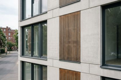 Unité de climatisation dissimulée derrière un cache en bois lamellé sur une façade d'appartement moderne en béton gris