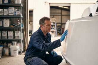 Technicien marine inspectant la surface en gel coat d'une coque de voilier dans un atelier de réparation nautique