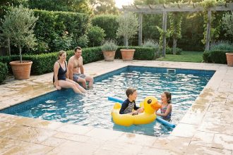 Famille profitant d'une piscine rectangulaire familiale dans un jardin avec terrasse en pierre naturelle et haies vertes